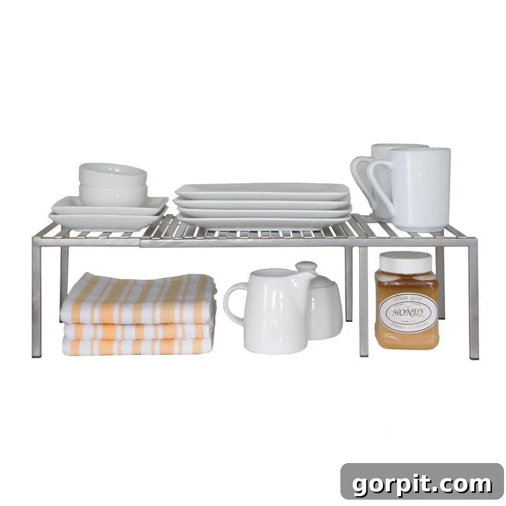 A product image of white wire expandable kitchen cabinet shelves with white plates and cups on top and yellow striped towels, milk holder, and bottle of honey. 