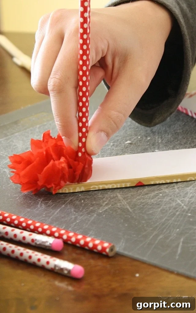 Continuously press tissue paper squares onto the glue-covered foam board using a pencil, filling the entire surface for a lush, fluffy DIY Valentine's wreath.