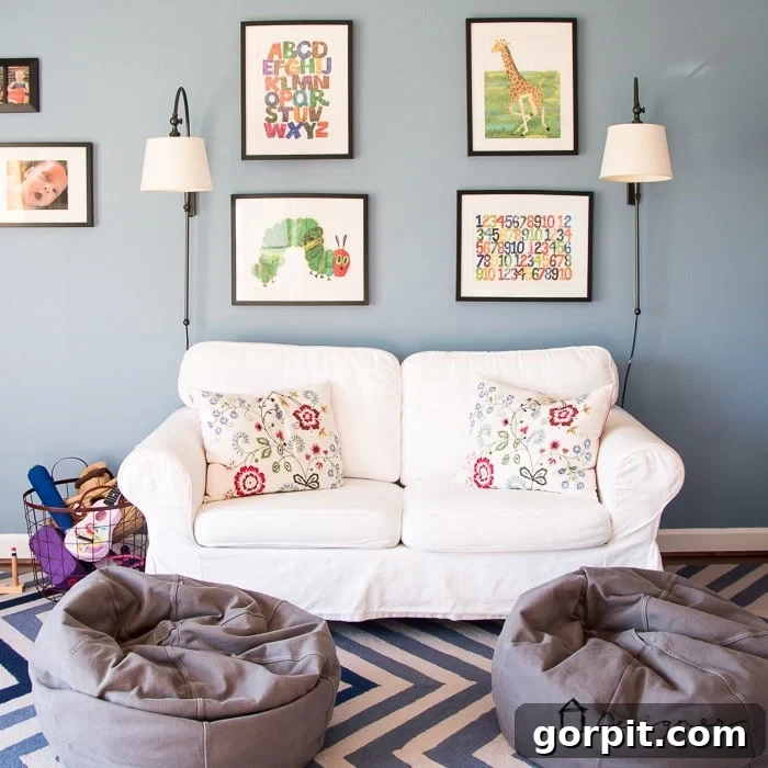 A playroom with blue-grey walls, a white loveseat and two child-sized bean bags. Framed children's book covers are on the wall. Good playroom ideas include comfortable seating.