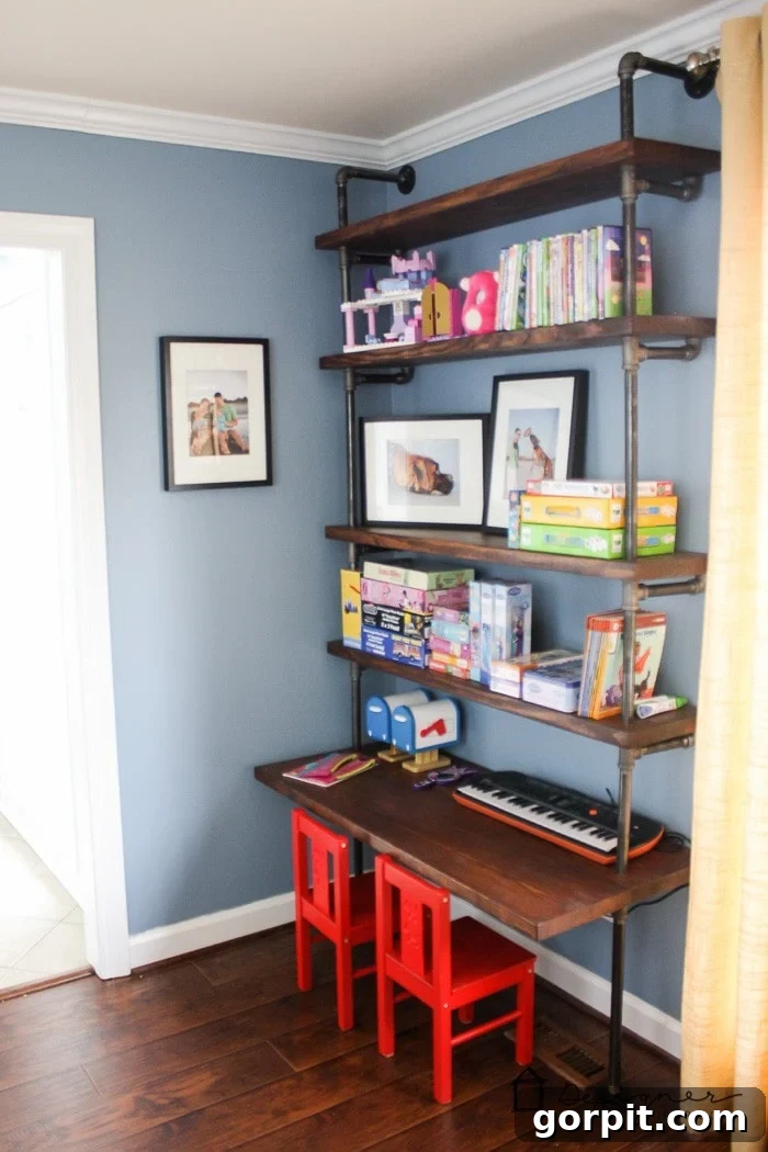 The corner of a playroom with pipe bookshelves and a shelf-desk. Books and games are neatly arranged on the dark wood shelves. 