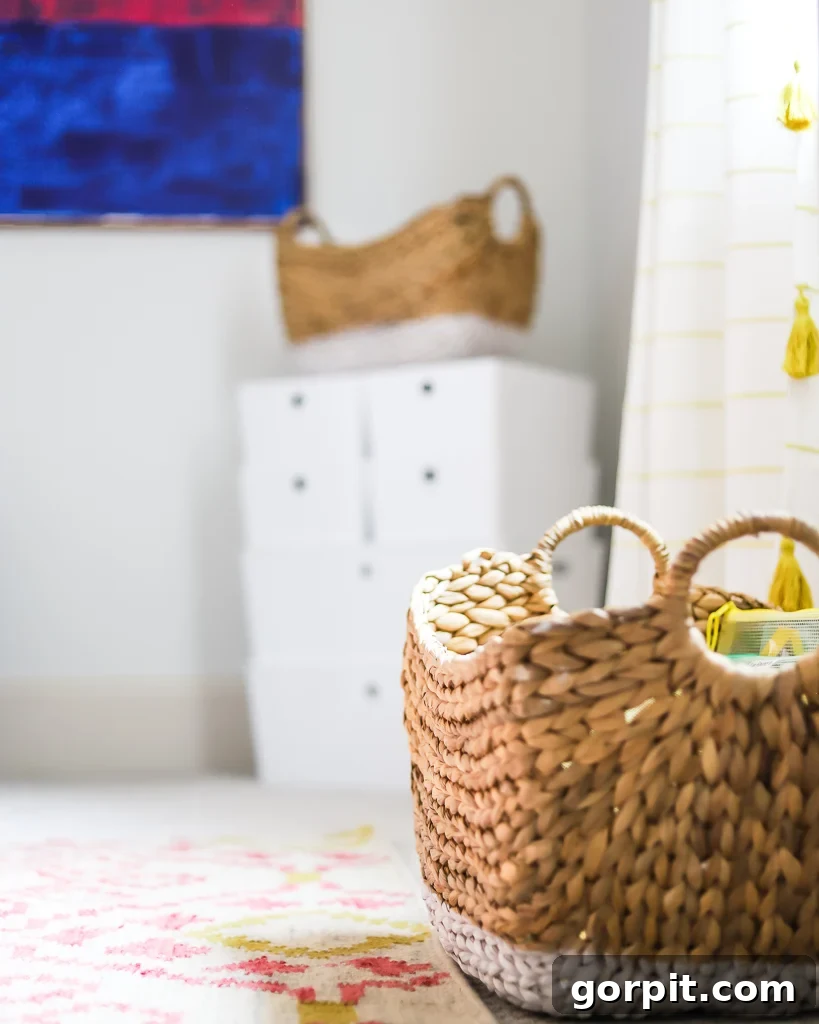A closeup of the corner of a weaved basket on a light, colorful rug. Blurry storage bins and a bright blue square painting are in the background. 