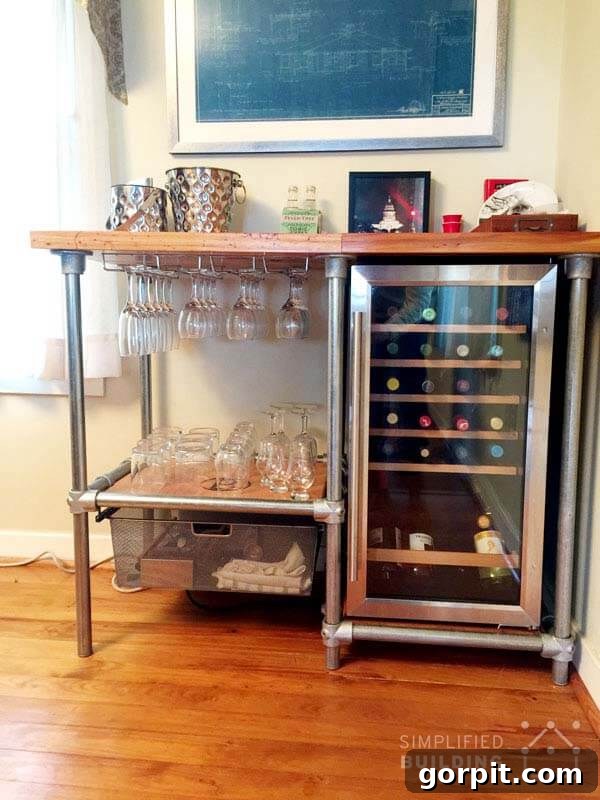 DIY industrial bar constructed with pipe shelving, featuring a mini-fridge and hanging glass storage