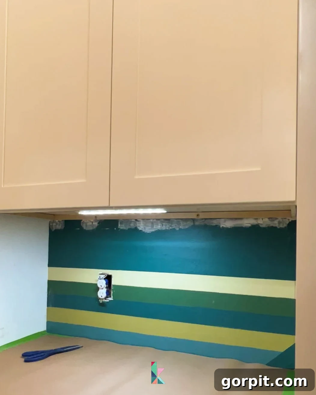 Preparing walls for tile backsplash installation, showing a clean surface and minor drywall repairs completed below an upper cabinet for a smooth foundation.
