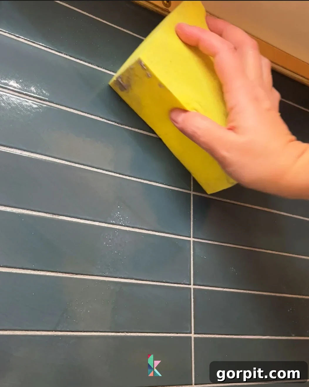 Wiping excess grout off of backsplash tile with a damp sponge, a crucial step for achieving a clean and professional-looking tile surface after grouting.