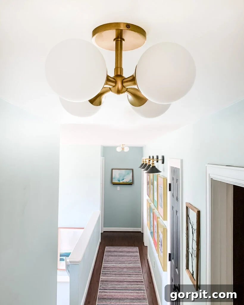 A modern white semi-flush mount light fixture featuring four round glass globes on a gold-colored mount, illuminating a bright hallway.