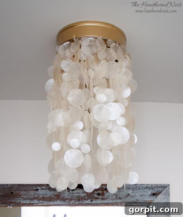 A close-up view of a stunning DIY light fixture featuring a circular capiz shell shade with delicate gold hardware, mounted flush against a pristine white ceiling.