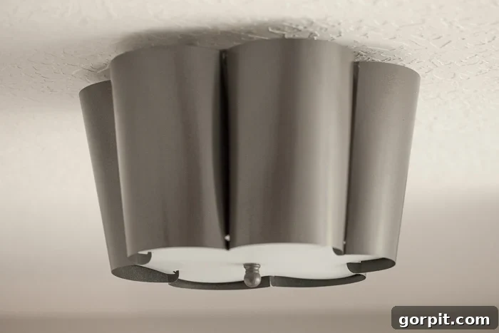 A simple white flush mount light fixture, dramatically transformed with metallic grey spray paint, mounted against a bright white ceiling for a modern, industrial look.