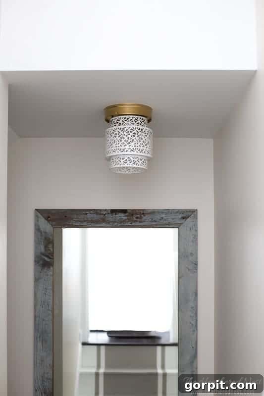 A captivating light fixture in a hallway, featuring an ornate white Moroccan-style metal lantern with gold hardware, replacing a standard dome light.