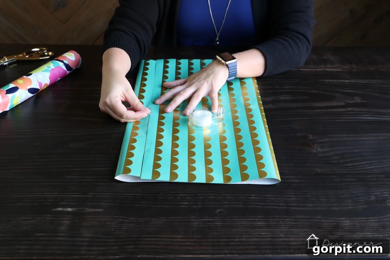 Folding and taping the sides of the wrapping paper to start forming a DIY gift bag, showing the initial seam creation.