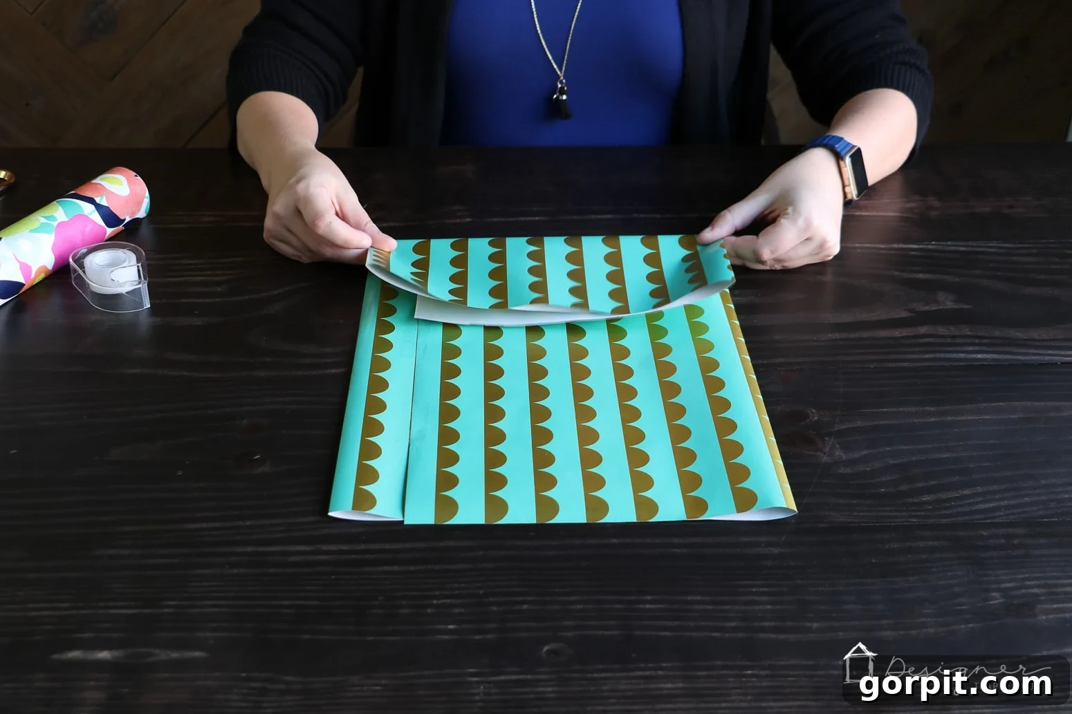 Folding the bottom edge of the wrapping paper upwards to create the initial base for a homemade gift bag.