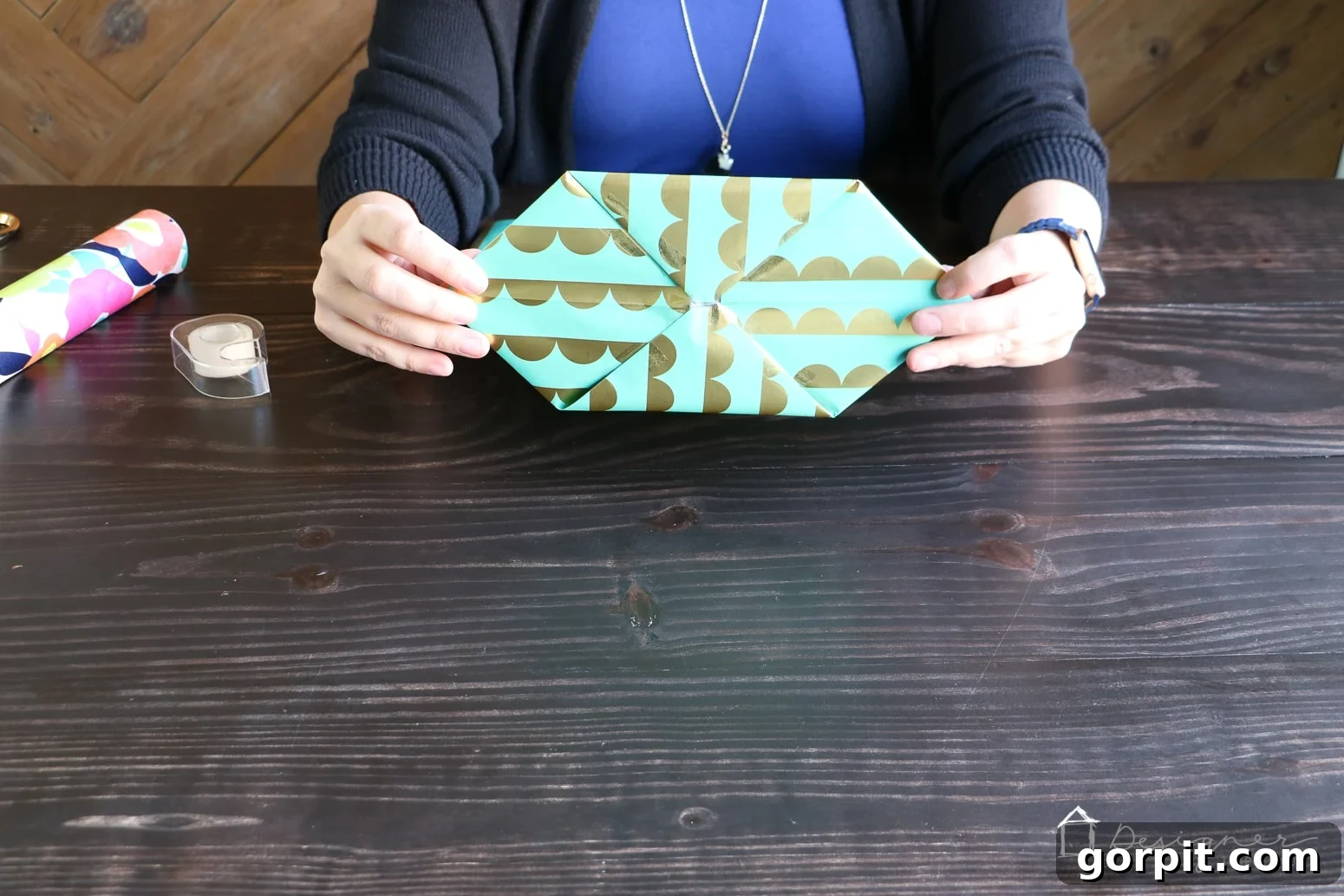 Taping the folded diamond shape at the bottom of the wrapping paper to complete and secure the base of the DIY gift bag.