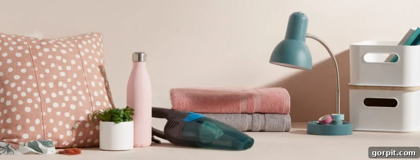 A neutral desk features dorm room ideas from Walmart, a sage dorm lamp, neutral folded towels, a water bottle, small plant, white bins, and other dorm room essentials.