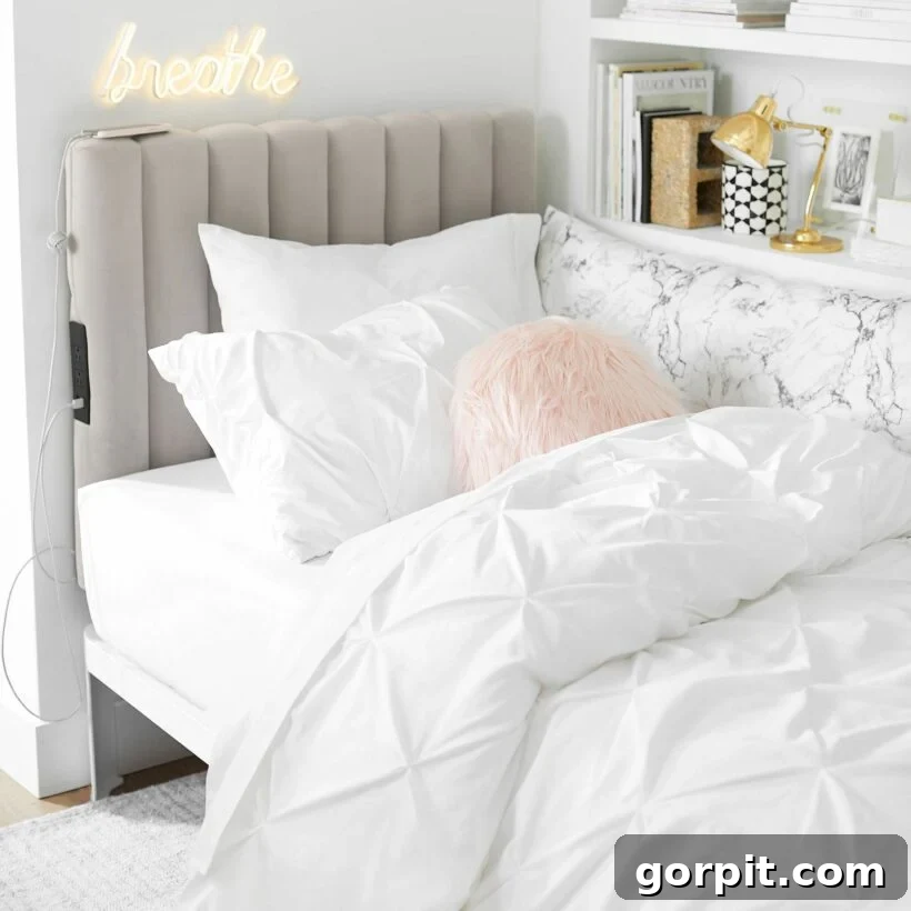 Pottery Barn offers dorm room ideas to make the most of the limited space such as this quilted headboard that charges devices, that is behind an all white bed and a full white bookcase.