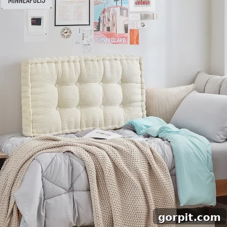An off-white tufted headboard on a dorm bed, with beige comfy blankets and some wall art and memorabilia as seen on Wayfair's dorm room ideas category.