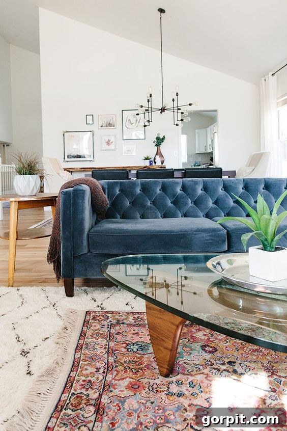 photo showing blue velvet sofa with two legs placed on larger area rug that has a smaller oriental rug layered on top of it