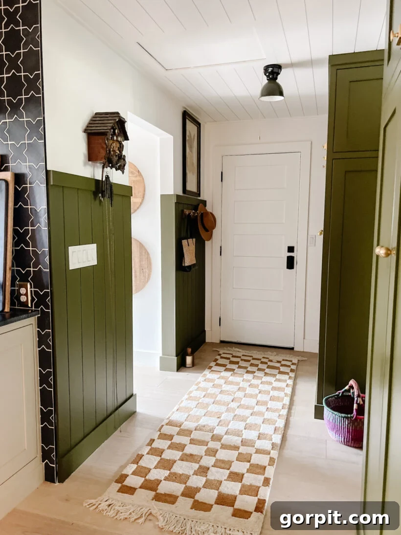 Elevate Your Interiors Innovative Accent Wall Designs 14 A shiplap accent wall in a hallway painted olive green covers more than half the height of the otherwise white walls, creating a chic and inviting entryway. A beige and white checkered runner is in the foreground.