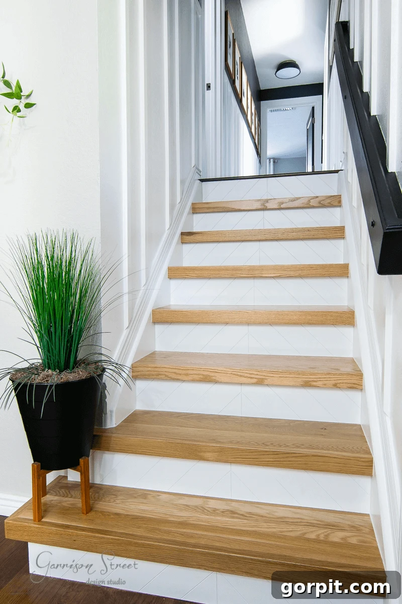 A staircase with rich wood treads, crisp white trim, and a chunky black stair rail on a plank wall, creating a standout, modern yet timeless look.