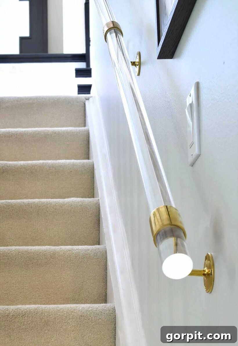 A clear Lucite handrail with elegant gold hardware creates an extremely eye-catching and unique design feature on a staircase, reminiscent of glass railings.