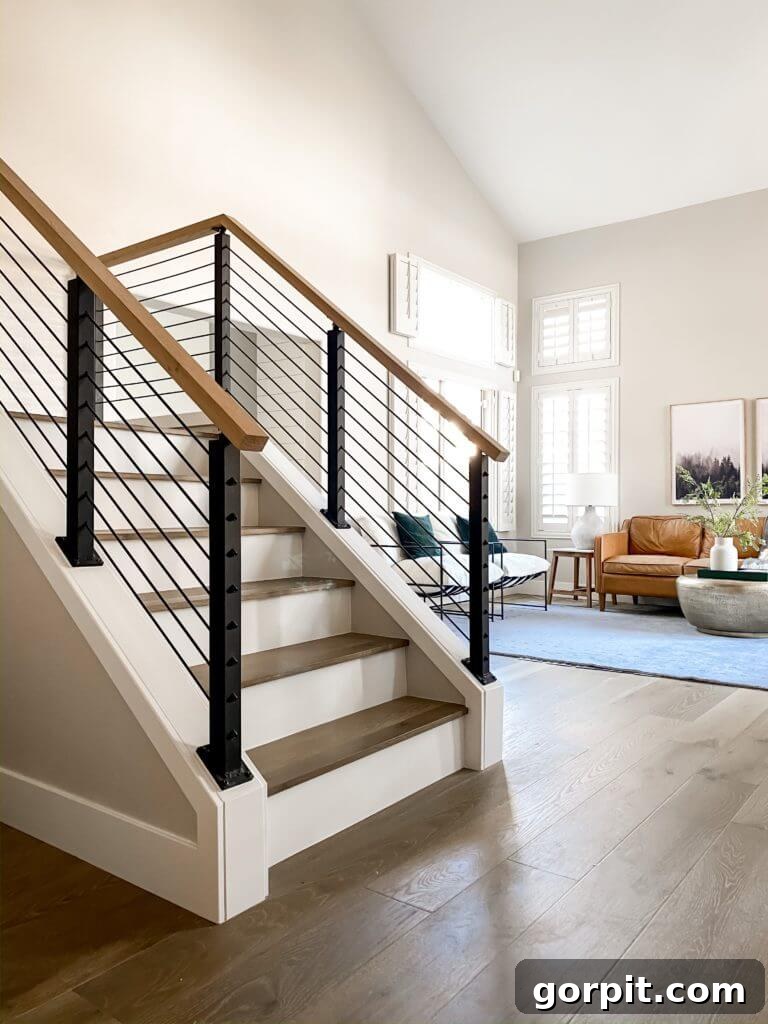 A sleek black cable railing modernizes white and wood stairs, creating an open feel into a living room.