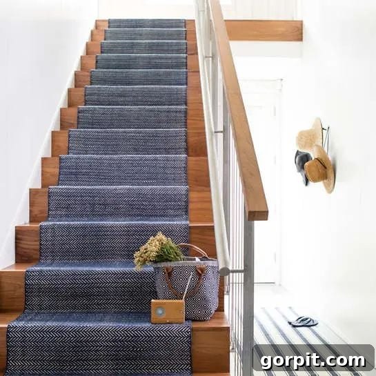 A wooden staircase with a blue carpet runner features a metal handrail, styled to feel warm and inviting, balancing industrial and natural elements.