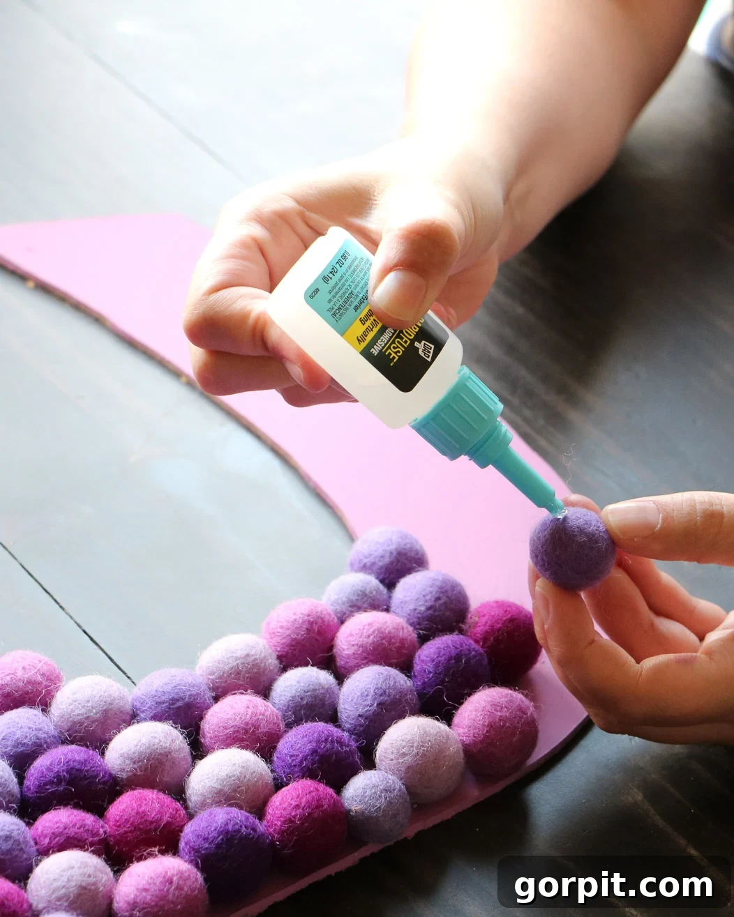 Elevate Your Decor with Handmade Giant Letters 7 Woman meticulously gluing colorful felt balls onto a DIY wall letter using RapidFuse adhesive