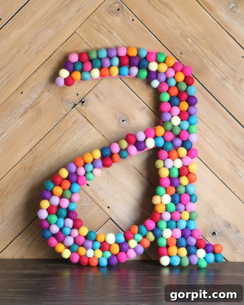 Elevate Your Decor with Handmade Giant Letters 9 A large, personalized wall letter 'A' adorned with colorful felt balls, enhancing a child's room decor.