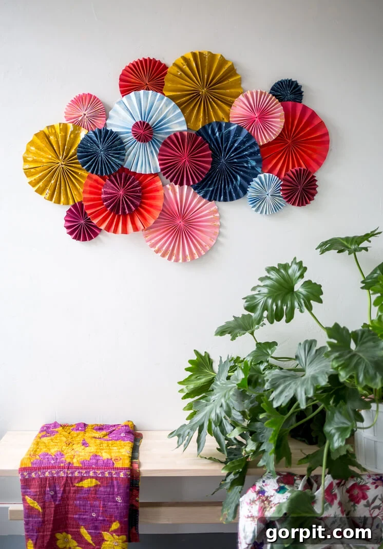 layered fan art made from bright colored card stock and gold paint over a bench with a kantha quilt and plant