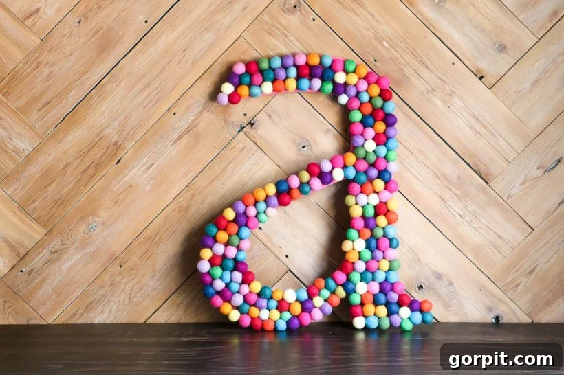 large DIY rainbow felt ball letter leaning on a wood wall