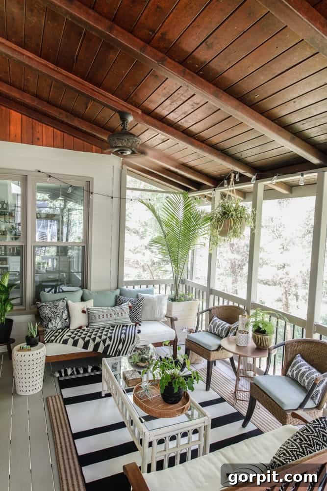 Screened Porch Dreams: Craft Your Perfect Outdoor Escape 11 A screened-in porch with a stained ceiling, black and white boho decor, a glass and wicker coffee table and lots of pillows, blankets and potted plants.