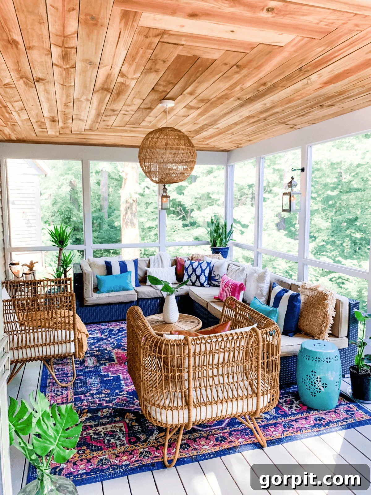 Screened Porch Dreams: Craft Your Perfect Outdoor Escape 12 This screened-in porch idea has a stained wood ceiling decorated with bright pinks and blues and rattan furniture on a bright area rug.