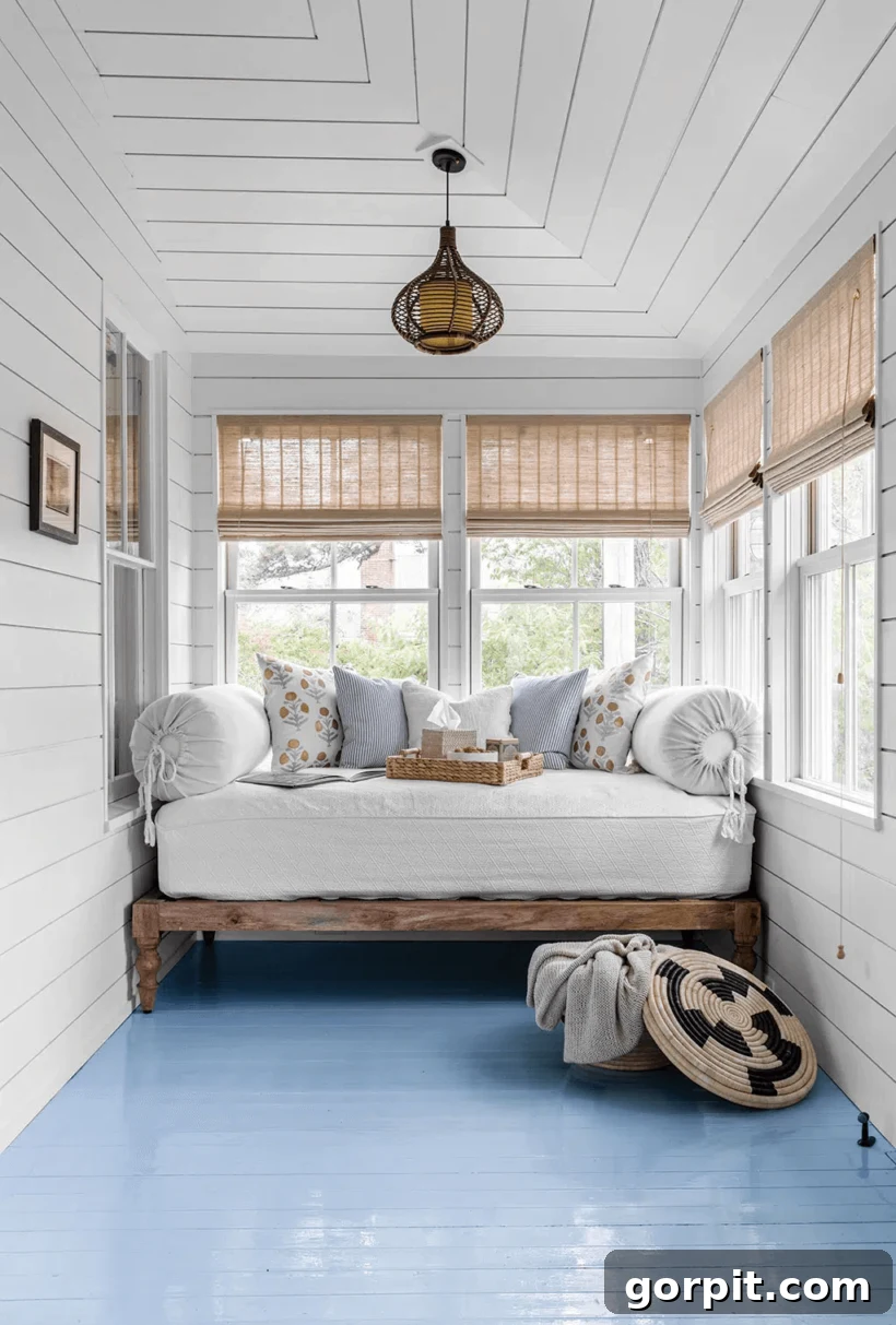 Screened Porch Dreams: Craft Your Perfect Outdoor Escape 7 A white sun porch with blue floor with daybed against the narrow back wall.