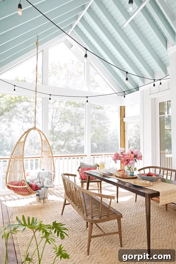 Screened Porch Dreams: Craft Your Perfect Outdoor Escape 9 Bright and airy screened-in porch idea features a vaulted ceiling painted light blue, string lights, a wooden dining table with bench seating, and a hanging wicker chair with colorful cushions.