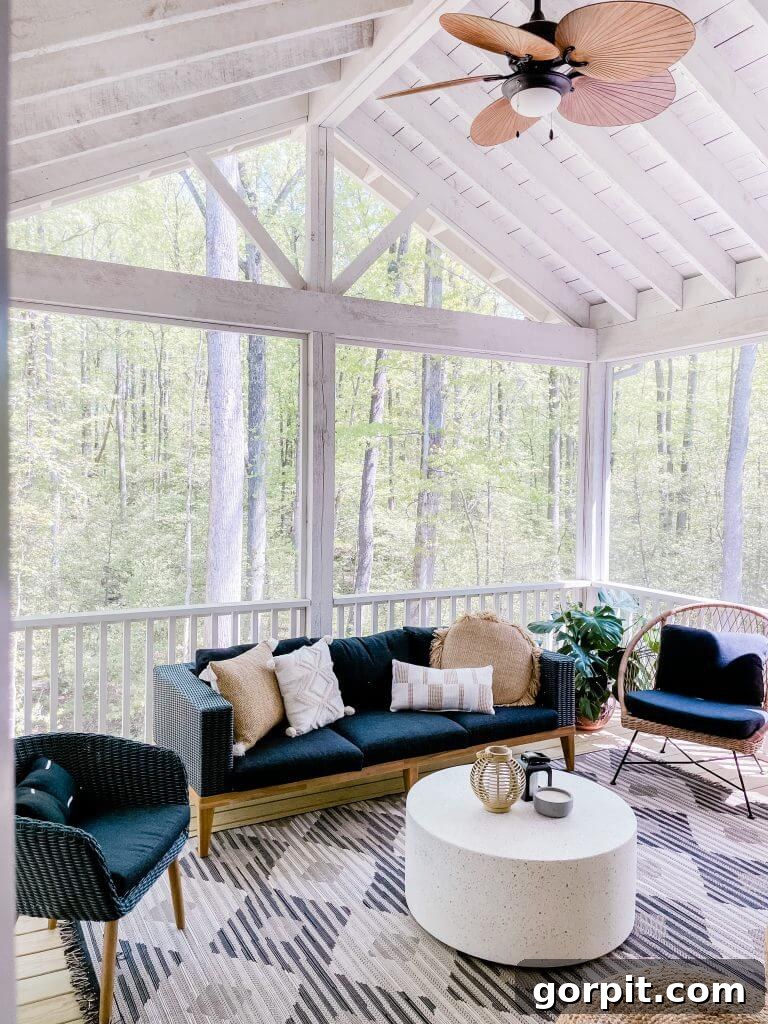 Screened Porch Dreams: Craft Your Perfect Outdoor Escape 10 One screened-in porch idea uses a wicker ceiling fan and black and white decor, surrounded by trees. A round white coffee table provides a central focus.