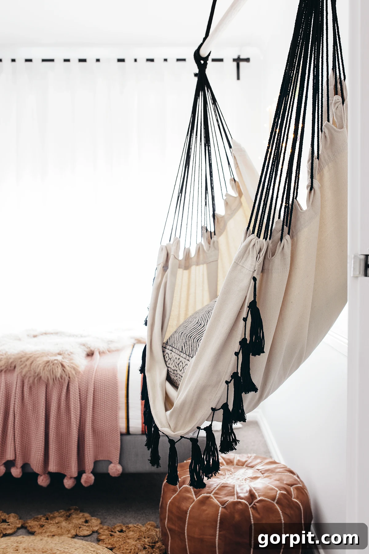 25 Fresh Teen Room Makeover Ideas for Guys and Girls 21 A comfortable hanging hammock chair is showcased in a teen girl's bedroom, positioned near a bed with a muted pink comforter, and a stylish leather pouf rests underneath, creating a cozy and inviting nook.
