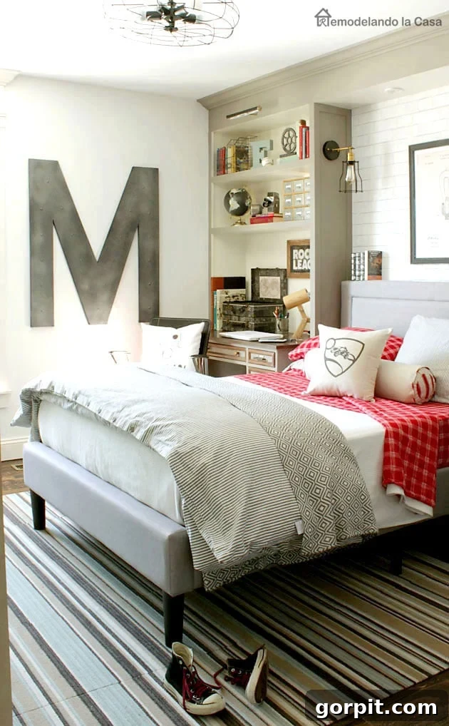25 Fresh Teen Room Makeover Ideas for Guys and Girls 30 An industrial teen boy's bedroom features a giant 'M' prominently displayed in the far corner. White brick walls flank built-in bookcases on either side of the bed, seamlessly integrating a functional desk, creating a cohesive and stylish space.