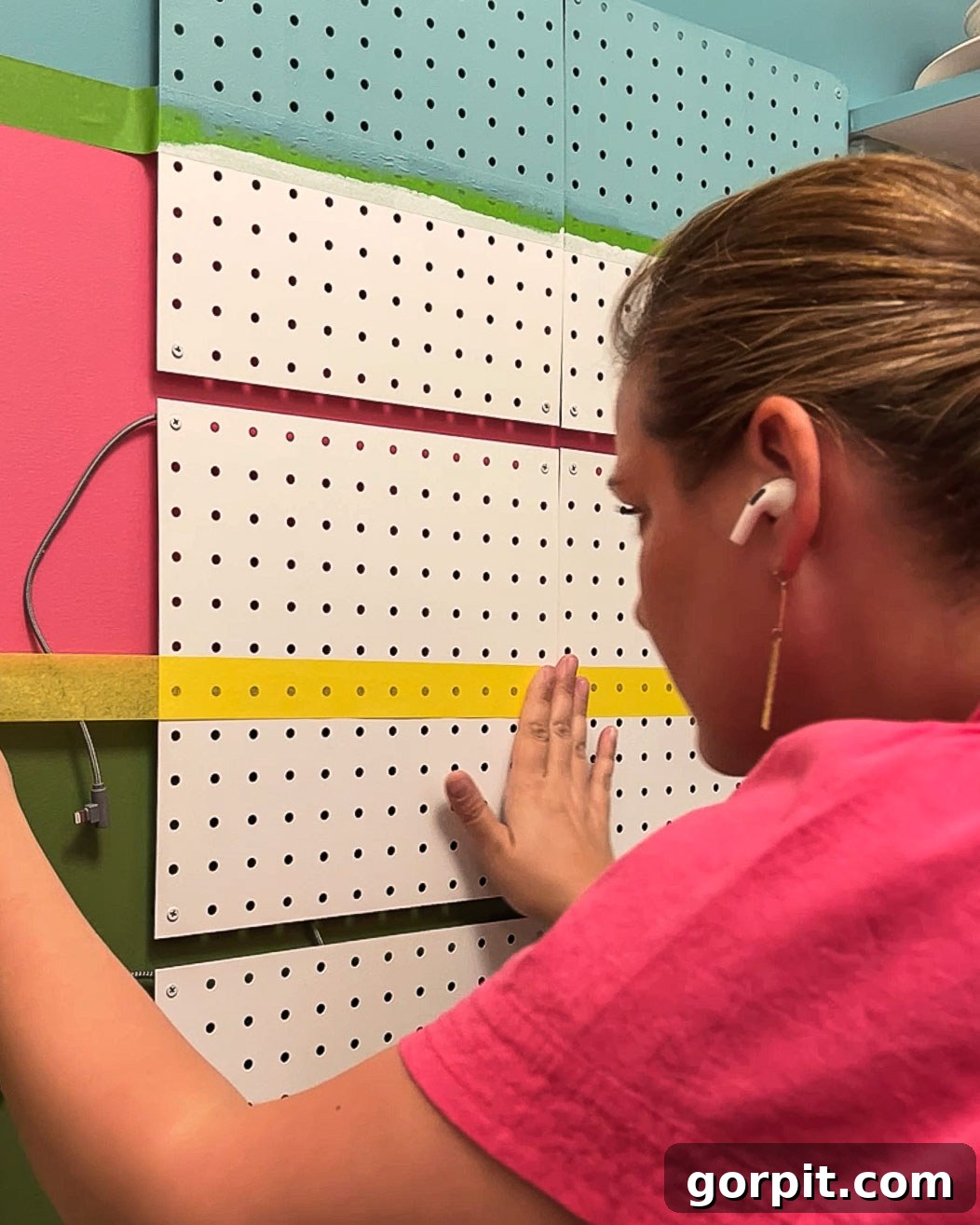 Woman painting striped metal pegboard to match a wall mural