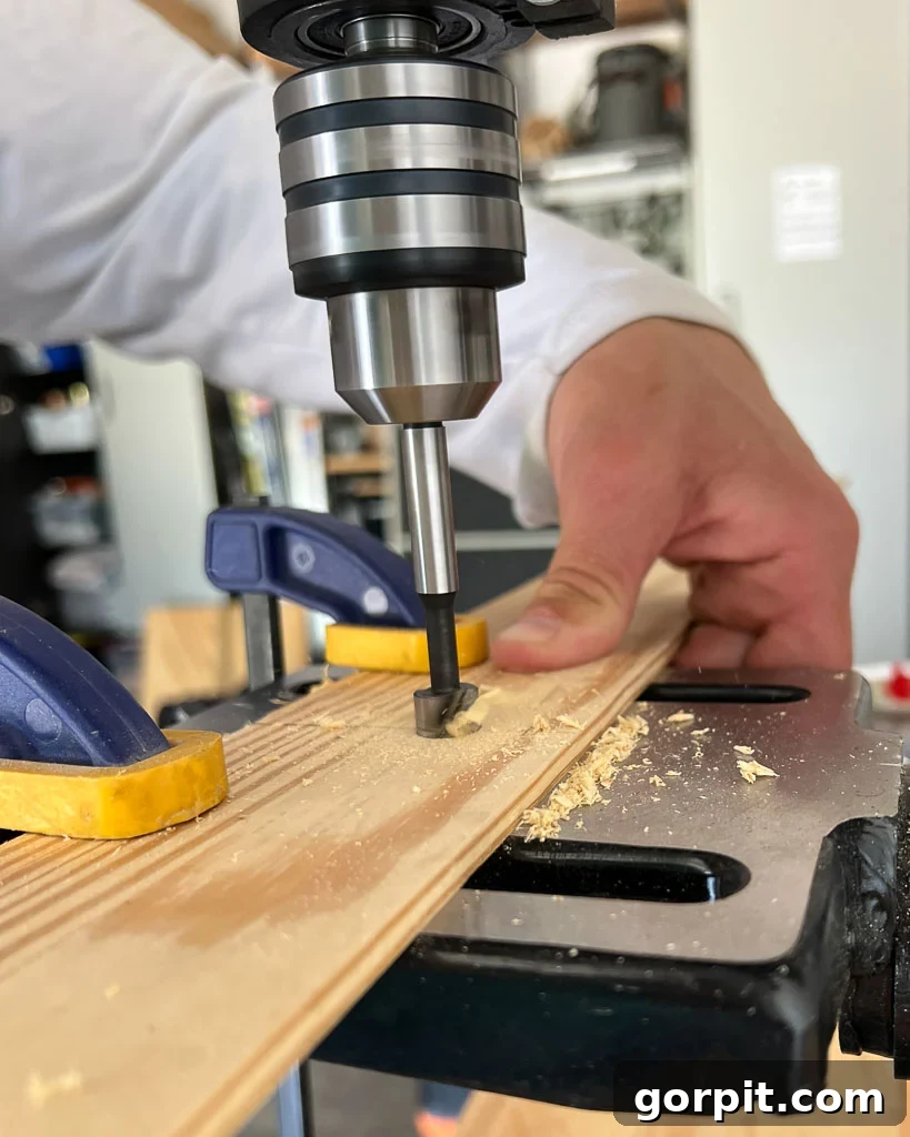 Forstner bit drilling into a wood strip to create a perfect recess for a magnet, demonstrating precision in DIY poster hanger construction.