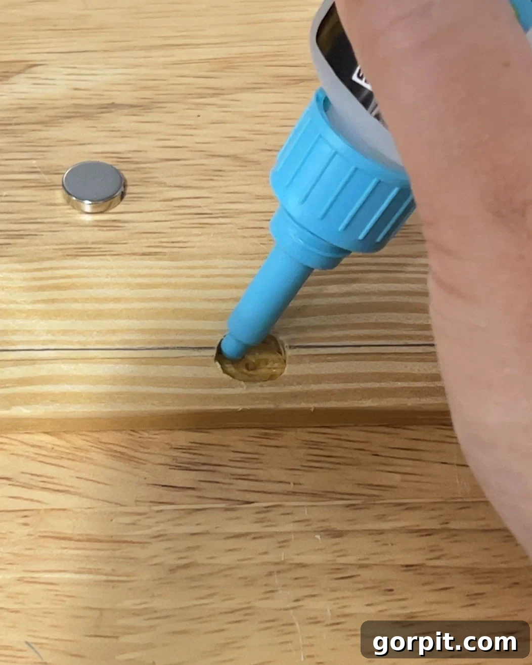 Close-up of gluing small, round magnets into a pre-drilled wood strip, emphasizing the careful placement required for magnetic poster hangers.