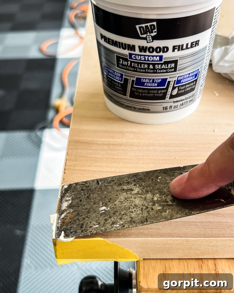 putty knife filling in imperfections plywood with wood filler