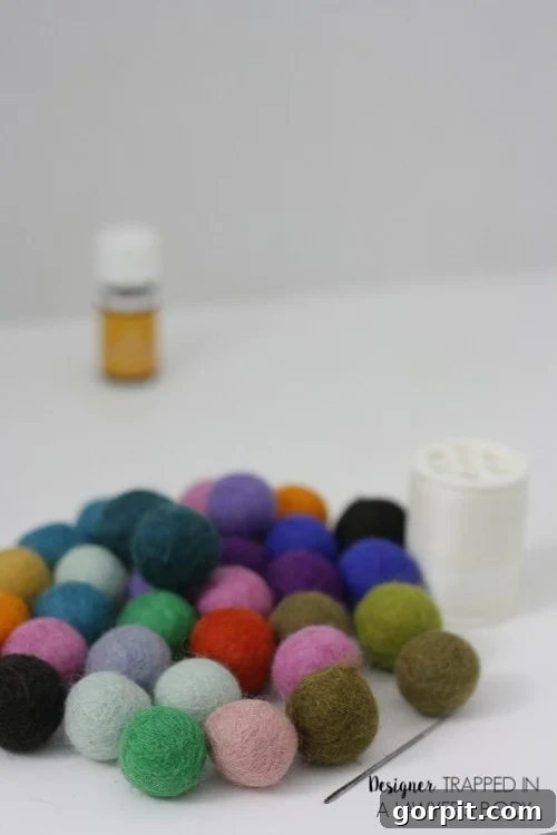 A group of many-colored felted balls on a white background with white thread and a needle. The text in the bottom right corner reads, 