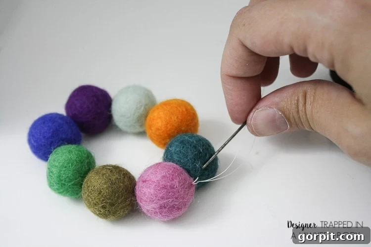 A woman's hand pulls a needle and thread through the last two felted balls forming a circle. This craft is from 