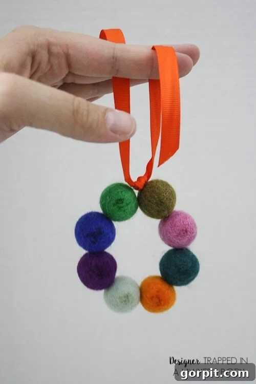 A DIY car air freshener is held by a woman's hand. The scented craft is made from a circle of feted balls hung on an orange ribbon. 