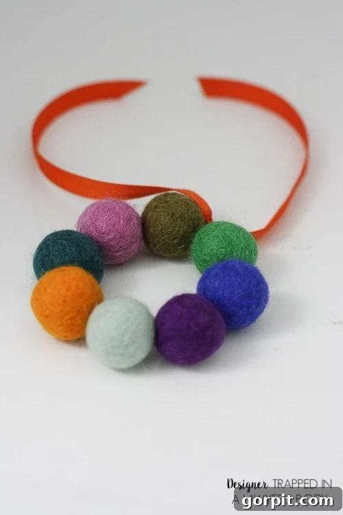 A close-up of the finished DIY car air freshener made from felt balls, an orange ribbon and essential oils. 