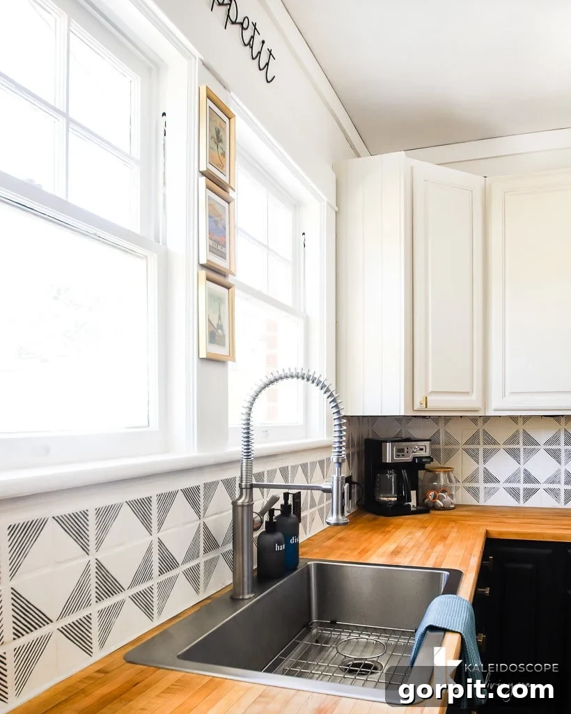 Kitchen with warm butcher block countertops and a beautifully painted and stenciled tile backsplash in a sophisticated black and white pattern, showcasing a budget-friendly and custom tile makeover solution.