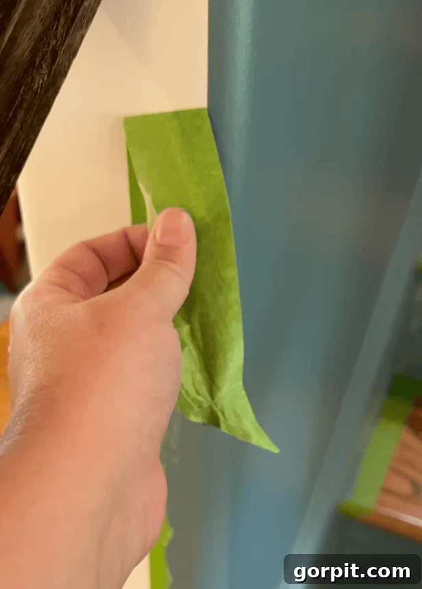 Photo of a hand gripping and carefully peeling a piece of yellow painter's tape off a wall, revealing a perfectly crisp and clean line where two distinct paint colors meet, showcasing the success of precision painting.