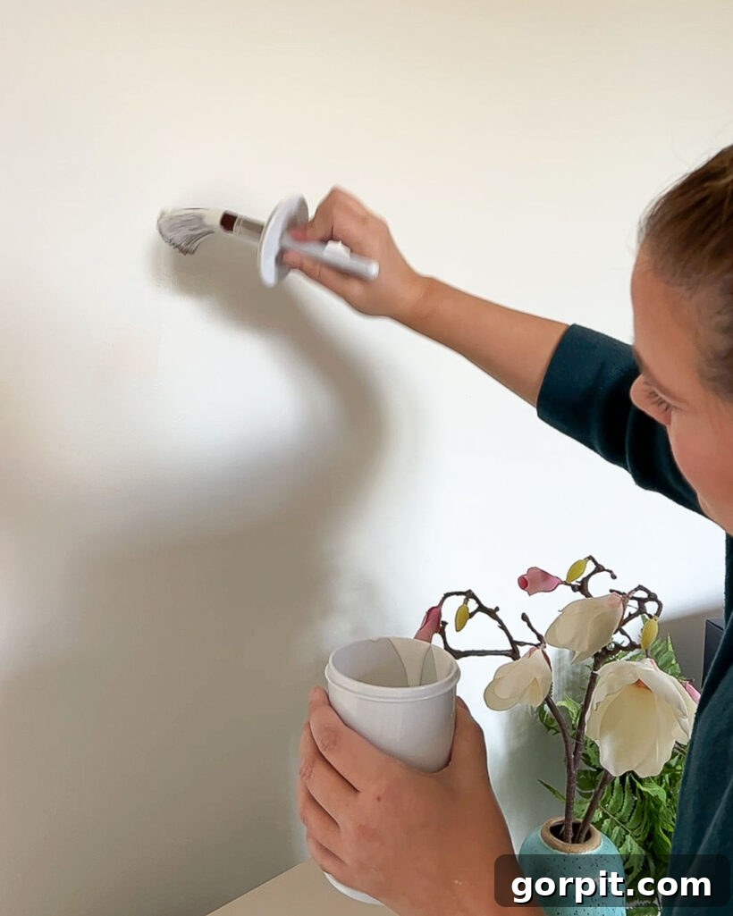 Tasha Agruso of Kaleidoscope Living expertly touching up white wall paint using a Paint Saint container with its integrated brush, demonstrating the simplicity and efficiency of quick paint fixes.