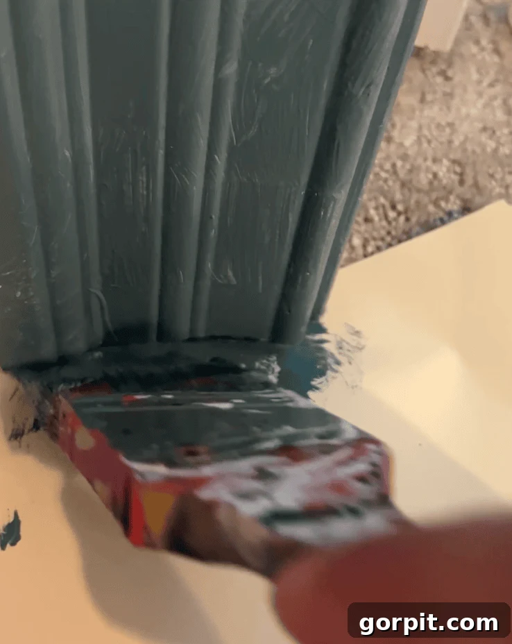 Close-up photo view of a paintbrush painting trim along a carpeted floor, with a simple manila file folder placed precisely under the edge of the trim to protect the carpet from any paint drips or splatters, showcasing an efficient painting hack.