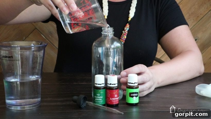 Homemade Chemical-Free Bug Defense 5 Pouring water into the witch hazel mixture, preparing the base for an all-natural DIY essential oil bug repellent.