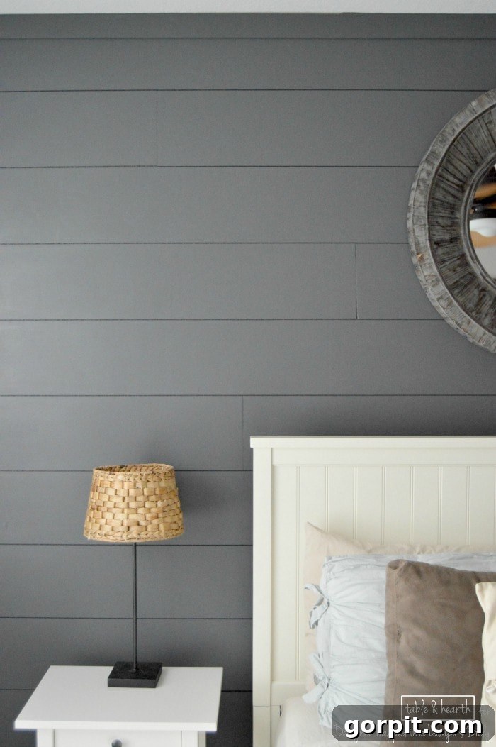 An inviting bedroom with a dark wood plank accent wall, styled with neutral bedding and decor
