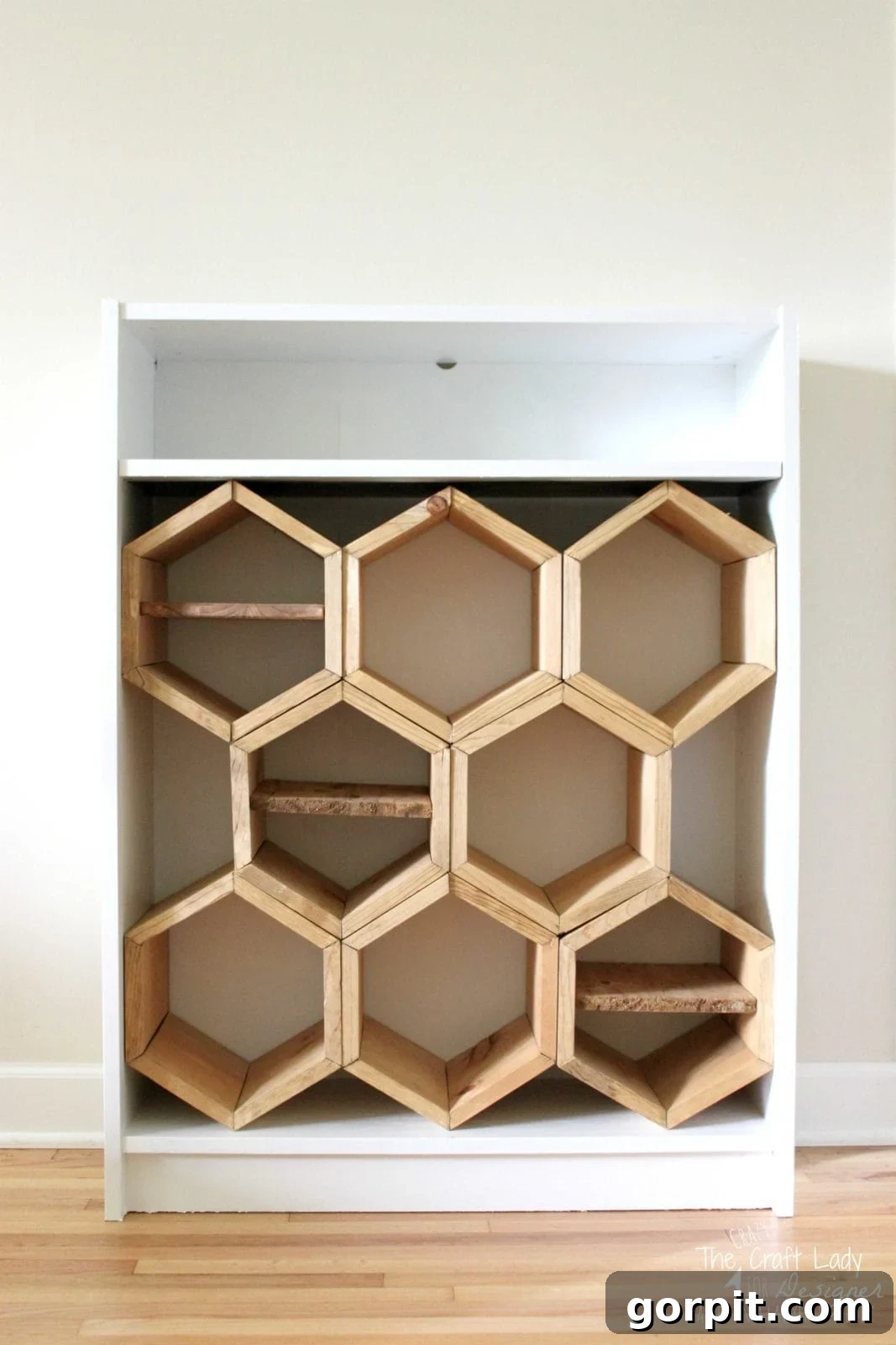 Honeycomb Shoe Rack DIY 16 A white bookcase has one shelf on top, but the remaining space is filled with a DIY shoe rack made from hand-cut hexagonal shoe cubbies, three of which have a wooden divider inside the honeycomb.
